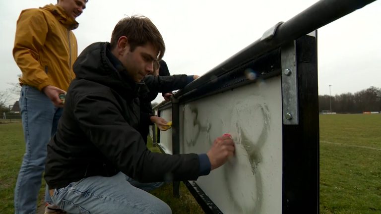 Voetballers HJSC poetsen graffiti van reclameborden Heeg
