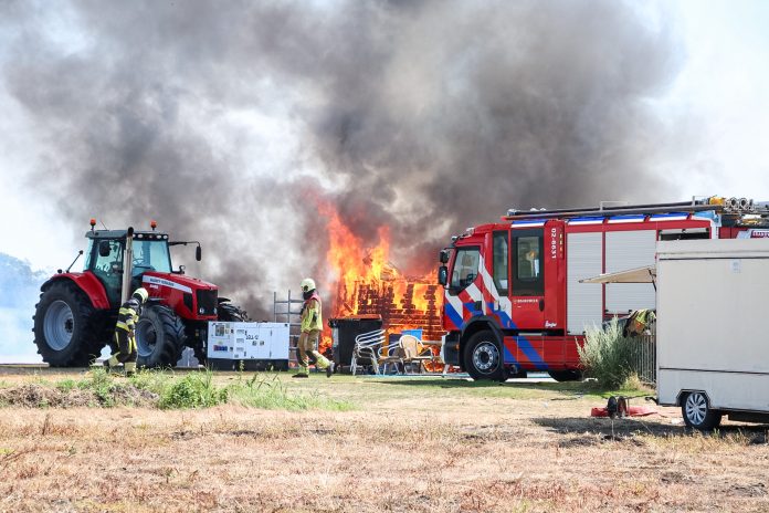 De brandweer probeert overslag naar een naastgelegen tractor te voorkomen.