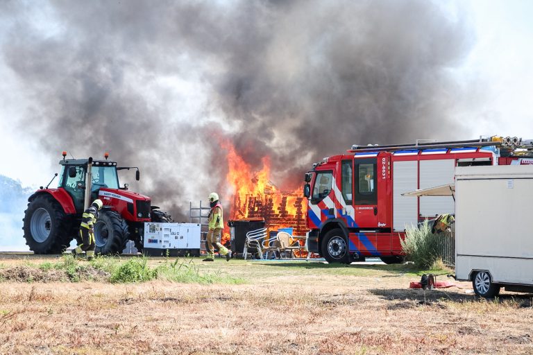 De brandweer probeert overslag naar een naastgelegen tractor te voorkomen.